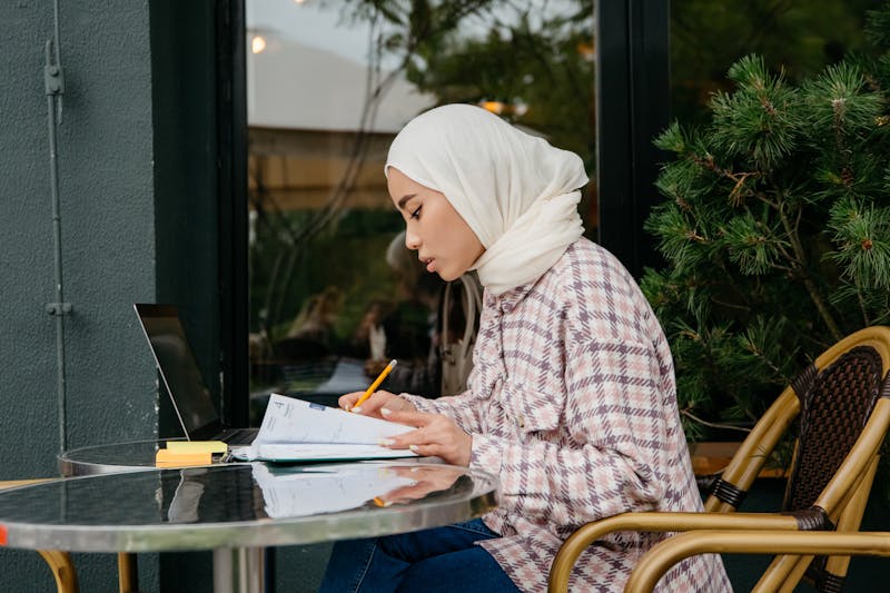 Young woman in hijab studying with notebook and laptop
