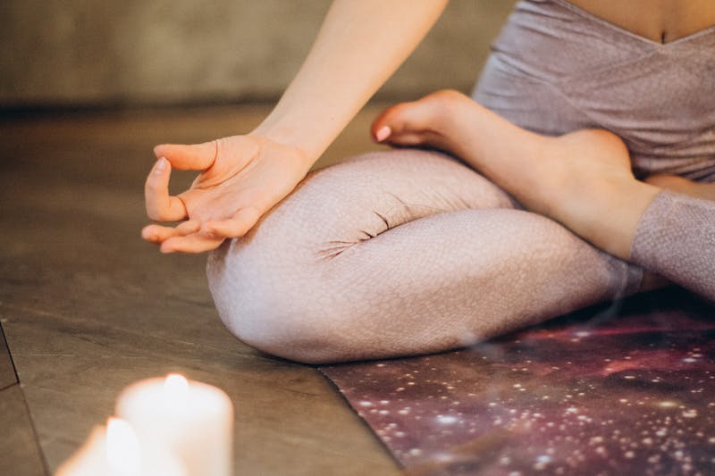 Person meditating in lotus position with candle